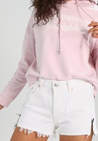Felpa rosa con logo "Levi's" bianco, abbinata a pantaloni denim bianchi con orlo frangiato e lati con zip.