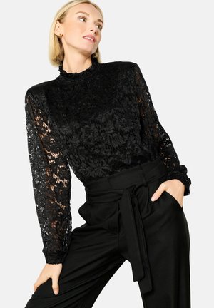 Black lace top with long sleeves featuring a high neck and textured design, paired with black, high-waisted pants and a fabric belt.