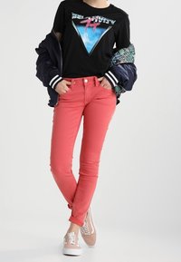 Camiseta negra con gráfico, jeans rosa ajustados y zapatillas claras. La chaqueta tiene forro con un patrón. Diseño sencillo, ajuste casual.