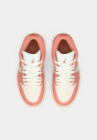 Baskets de sport roses clair et crème avec une boîte à orteils perforée, des lacets blancs et un logo discret sur la languette et les côtés. Texture en cuir lisse.