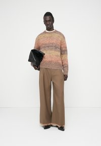 Πλεκτό πουλόβερ πολύχρωμο με μοτίβο βαθμιδωτών αποχρώσεων, συνδυασμένο με μπεζ παντελόνια φαρδιάς γραμμής και μαύρη τσάντα. Η εμφάνιση περιλαμβάνει στρογγυλή λαιμόκοψη.