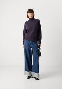 ņavy turtlenecks džemperis ar ribotām malām, apvienots ar plaša kāju ziliem džinsiem ar gaiši pelēku auduma aproci. Neitrāla rokassoma un melnas kurpes.