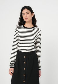 Μπλουζάκι μακρυμάνικο με ρίγες σε λευκό και μαύρο, με στρογγυλή λαιμόκοψη, σε συνδυασμό με μαύρη φούστα με κουμπιά μπροστά.