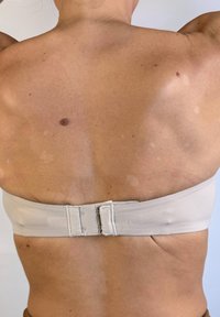 Sostén strapless de color beige claro con una textura suave y cierre trasero ajustable, que presenta un diseño minimalista y líneas limpias.