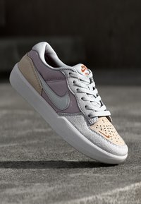 Nike copati z belim mrežastim in semiš zgornjim delom v vijolični in bež barvi, z perforacijami, svetlo modrim swooshom in oranžnimi logotipnimi akcenti.