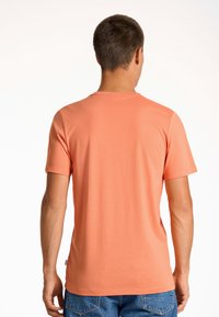 Kortärmad t-shirt i korall, tillverkad av mjukt tyg. Rund hals, enkel design, lätt stretch. Buren med blå denimjeans.