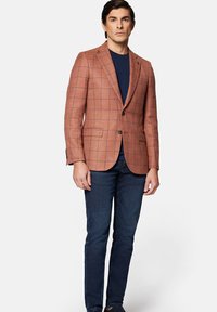 Brązowa marynarka w kratę z teksturowanej tkaniny, z dwiema przednimi kieszeniami, zapięciem na pojedynczy guzik oraz klapami, w połączeniu z granatowym t-shirtem i dżinsami.