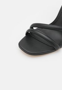 Sandale noire avec bout carré et deux fines brides sur le dessus du pied, présentée sur fond blanc.