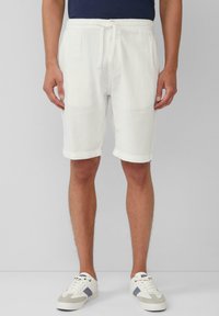 Weiße Leinen-Shorts mit elastischem Bund und Kordelzug. Glatte Textur, knielanges Design und umgeschlagener Saum. Getragen mit weißen Turnschuhen.