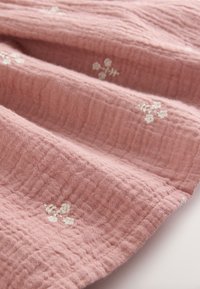 Tessuto rosa con motivo testurizzato e ricamo floreale bianco, che mostra un aspetto morbido e stropicciato e una caduta delicata.