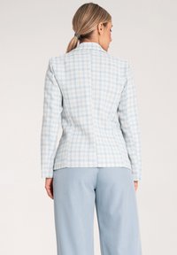 Jasnoniebieska marynarka w kratę o dopasowanym kroju, z długimi rękawami i klapami. Stylizowana z dopasowanymi szerokimi spodniami w jasnoniebieskim kolorze.