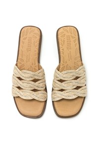Sandalias planas beiges con un diseño superior trenzado. Presentan acentos plateados y una plantilla de cuero marrón con un patrón. Punta cuadrada y suela marrón.