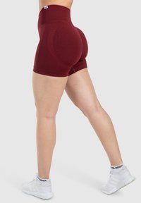 Pantaloni corti a vita alta di colore bordeaux realizzati in tessuto elastico. Presentano un design senza cuciture, cuciture a contrasto e una vestibilità aderente.