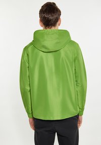 Kort grön vattentät jacka med huva, med en slät, något reflekterande yta och elastiska ärmslut, sedd från baksidan.