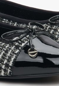 Czarna lakierowana skóra na czubku buta z plecionym górnym materiałem w czarno-białe wzory. Posiada satynową kokardkę oraz metaliczny detal z przodu.