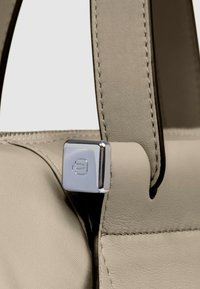 Sac à main gris avec une texture en cuir lisse, doté d'un accent en métal argenté à l'attache de la sangle. Détails de couture subtils visibles.