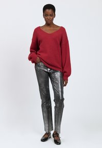 Maglione rosso oversize in maglia con scollatura a V profonda, abbinato a pantaloni dritti metallizzati argento con fessure laterali. Scarpe basse nere.