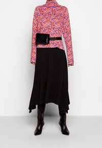 Färgglad mönstrad topp i rosa och lila med hög halsringning, tillsammans med en svart asymmetrisk kjol och knähöga svarta stövlar.