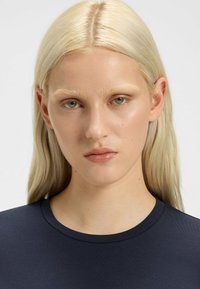 Modella con lunghi capelli biondo platino lisci, che indossa una maglietta aderente blu navy con scollatura tonda, con minima visibilità di texture e dettagli.