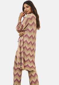 Conjunto de punto que incluye un cardigan largo y pantalones a juego con un patrón en chevron. Los colores predominantes son beige, rosa y verde, con un acabado texturizado.