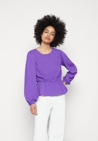 Blusa roxa de manga longa com decote redondo e cintura franzida. O tecido tem um padrão de riscas texturizadas e mangas bufantes.