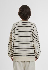 Maglione a righe in beige e blu navy. Vestibilità ampia con spalle scese, polsini a coste e collo rotondo. Texture lavorata a maglia, design casual.