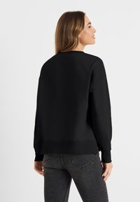 Zwart sweatshirt met lange mouwen, ronde hals en geribde manchetten. Zachte stoftextuur, comfortabele pasvorm en een gezette zoomdetail.
