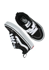 Zapatillas de lona negras con cordones blancos, detalles blancos y una pestaña roja en el talón. Presentan un diseño de caña baja y suela de goma texturizada.