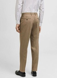 Pantaloni personalizați de culoare maro, cu o croială dreaptă, prezentând buzunare la spate cu închidere prin nasturi și o textură netedă. Pantofii asortați sunt negri.