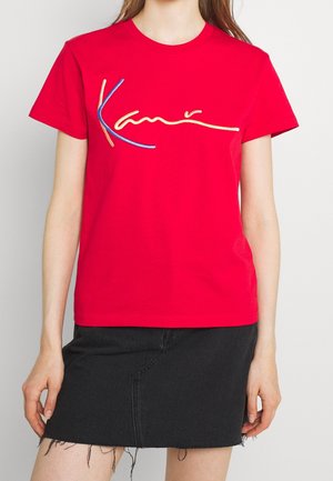 Rød bomuld T-shirt med flerfarvet broderet tekst "Kani" i blå, gul og orange; rund hals og korte ærmer.