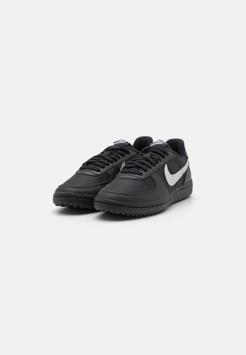Scarpe sportive nere con tomaia sintetica liscia, marchio grigio e suola in gomma testurizzata. Presentano un design con lacci e colletto imbottito.