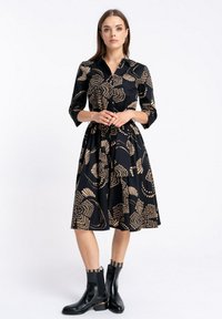 Czarna sukienka z rękawami do trzech czwartych i kołnierzykiem, z beżowym kwiatowym wzorem. Połączona z czarnymi botkami za kostkę.