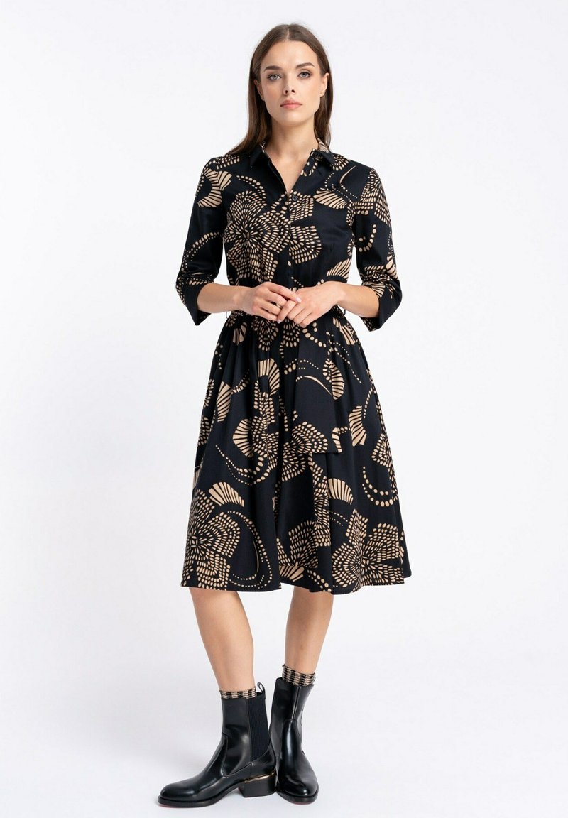 Czarna sukienka z rękawami do trzech czwartych i kołnierzykiem, z beżowym kwiatowym wzorem. Połączona z czarnymi botkami za kostkę.
