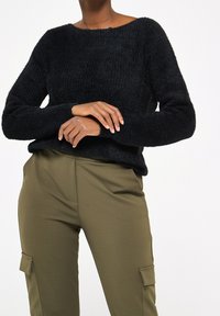 Černý huňatý svetr s širokým výstřihem a dlouhými rukávy, doplněný olivovými cargo kalhotami s kapsami na klopě a volným střihem.