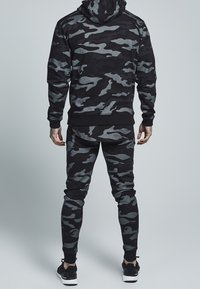 Black camouflage hoodie and matching tapered pants, made of textured fabric with gray accents and ribbed cuffs. Designed for comfort and fit.