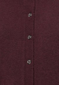 Cardigan en tricot bordeaux avec une fermeture à boutons à l'avant comportant cinq boutons foncés, des bords côtelés et un tissu doux et texturé.