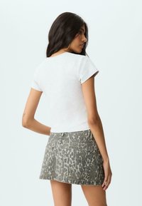 Grå kortærmet t-shirt parret med en grøn leopardprint denimnederdel. T-shirten har en tilpasset form, mens nederdelen har baglommer.