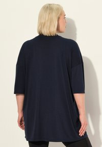 Tunika over-size blu scuro con maniche a tre quarti, caratterizzata da un collo rotondo e un tessuto morbido e liscio. Progettata con una vestibilità rilassata e spacchi laterali.