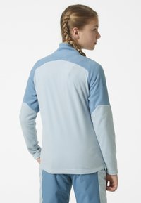 Jasnoniebieski polarowy sweter z wysokim kołnierzem, kontrastującymi ciemnoniebieskimi panelami na ramionach i długimi rękawami; miękka tekstura i luźny krój.