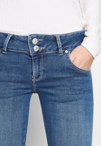 Blå denimjeans med stängning med två knappar, fem-fickorsdesign och subtila sömnadsdetaljer. Strukturerad tyg med en klassisk passform.