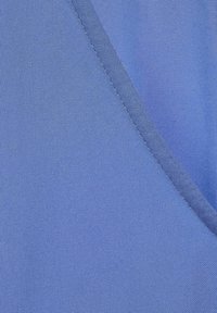 Tessuto blu con una texture liscia, caratterizzato da un dettaglio di cucitura diagonale. Il materiale sembra leggero e traspirante.