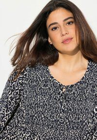 Blouse bleu marine avec un motif texturé crème, détail en trou de serrure au niveau du col et manches à coupe décontractée. Tissu lisse.