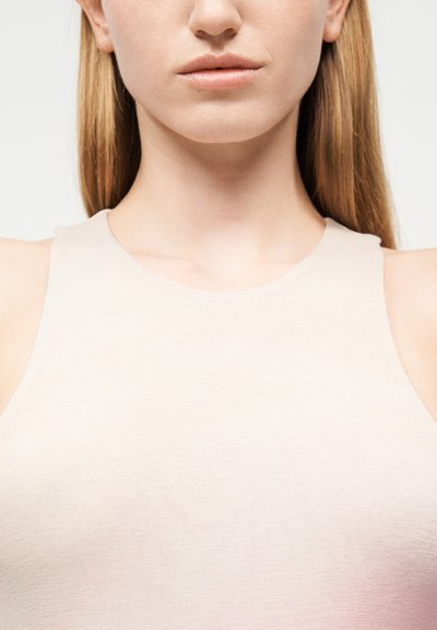 Κοντινό πλάνο του κάτω μέρους του προσώπου μιας γυναίκας, του λαιμού και των ώμων, που φοράει αμάνικη μπεζ μπλούζα με ίσια ξανθά μαλλιά, σε λευκό φόντο.