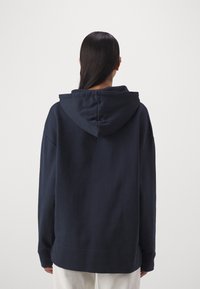 Mörkblå hoodie med avslappnad passform, dragsko i huvan och långa ärmar. Mjuk textur och ribbade ärmslut. Minimalistisk design utan mönster.