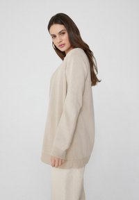 Beiger Strickpullover mit lässiger Passform, gerippten Bündchen und Saum, mit einer strukturierten Oberfläche. Weicher Stoff mit langen Ärmeln.