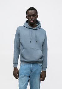 Lyseblå bomulds-hoodie med forlommer, snøre i hætten og ribkant ved ærmerne. Kombineret med lyseblå denimjeans.