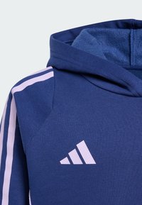 Tamno plavi dukserica s kapuljačom, ružičaste pruge na rukavima, teksturirana tkanina i izvezeno bijelo Adidas logo na prsima.