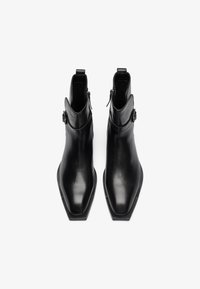 Botines de cuero negro con punta cuadrada afilada, diseño elegante, cremalleras laterales y un borde texturizado para un detalle adicional.