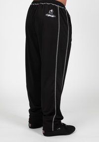 Black sweatpants with grey side stripes and elastic waistband. Features logo on the left side. Soft fabric with a relaxed fit.