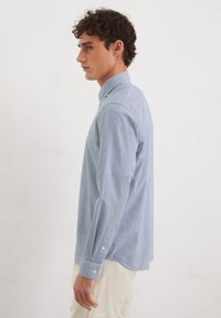 Himmelblau gestreiftes Hemd mit langen Ärmeln, abgerundetem Saum und geknöpften Manschetten. Strukturierter Stoff mit subtilen vertikalen Streifen.